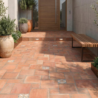Patio exterior con suelo rústico terracota Benisa, baldosas variadas y macetas.