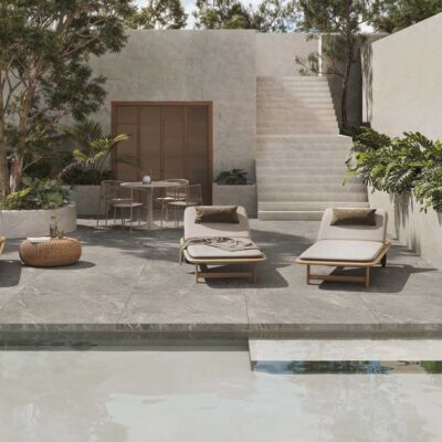 Terraza exterior moderna con piscina y tumbonas. El suelo porcelánico gris de acabado mate crea un ambiente elegante y funcional.
