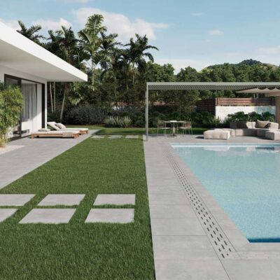 Suelo porcelánico imitación cemento Columbia Grey en patio y piscina de casa moderna con jardín.