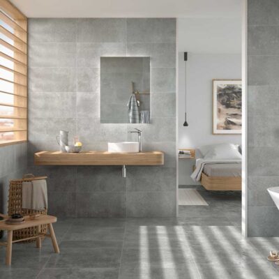 Baño moderno con suelo y paredes de suelo porcelanico efecto cemento claro. Mueble de madera, lavabo y bañera.