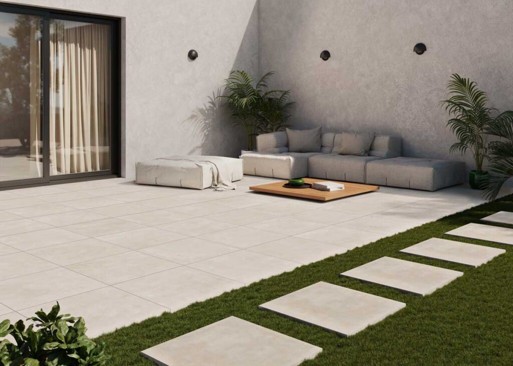 Patio exterior moderno con suelo porcelanico efecto cemento color arena. Incluye sofá y plantas.