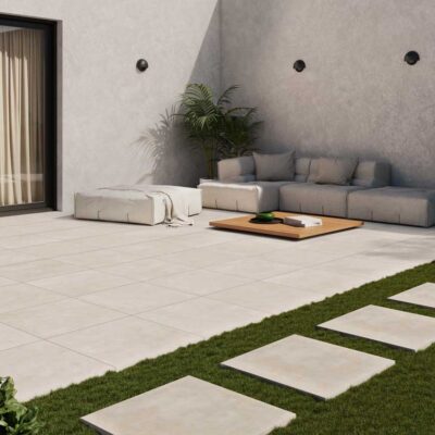 Patio exterior moderno con suelo porcelanico efecto cemento color arena. Incluye sofá y plantas.