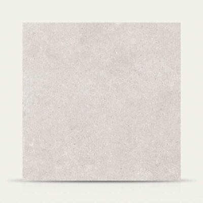 Una baldosa porcelánica efecto piedra Leiria Greige de tono greige claro sobre fondo neutro.