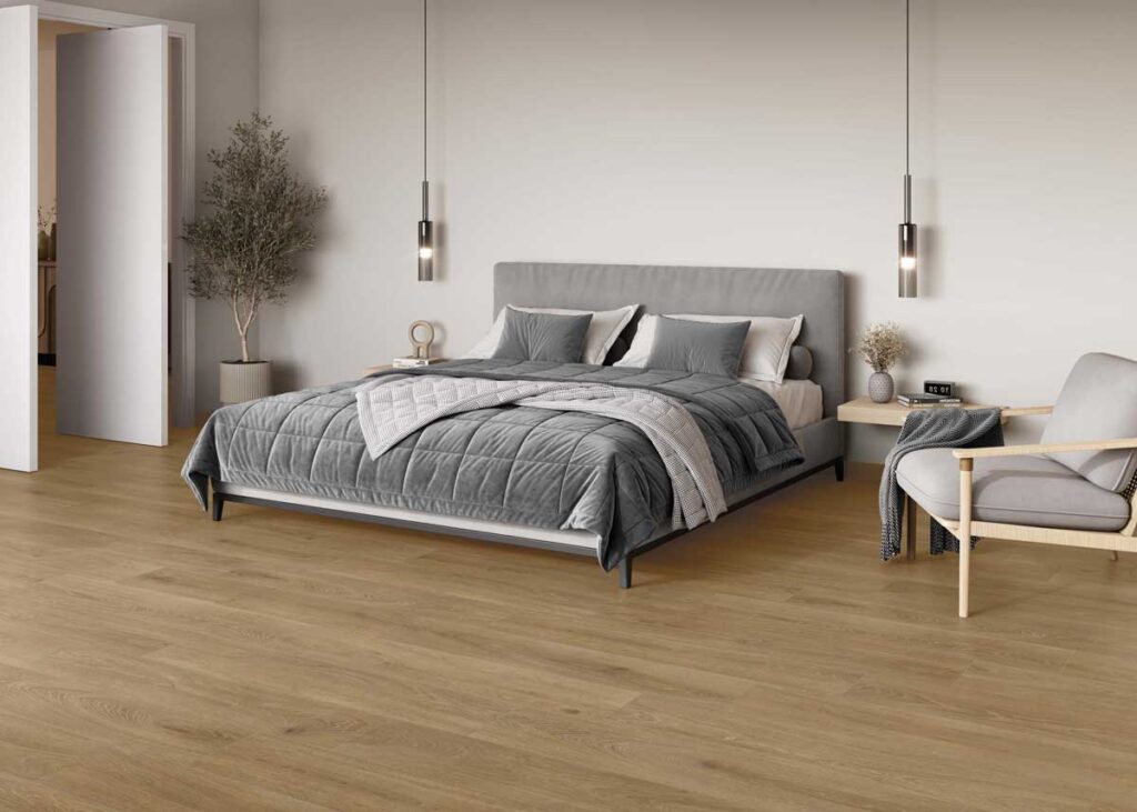 Dormitorio moderno con suelo porcelánico imitación madera Haspe Roble, cama gris y planta.