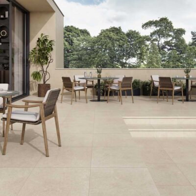 El suelo porcelánico Leiria Natural claro cubre una terraza exterior con mesas y sillas.