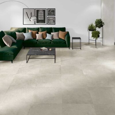 Salón moderno con suelo porcelánico efecto cemento Lorraine Sand. Sofá verde y mesa negra.
