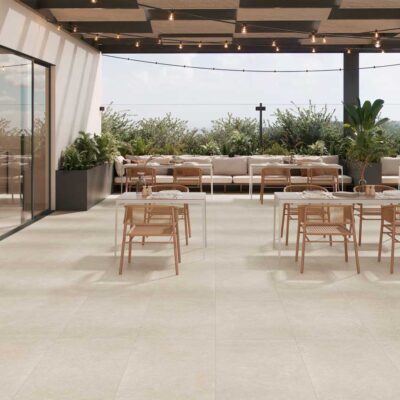 Terraza exterior de restaurante con suelo porcelánico efecto cemento Leiria Natural, mesas y plantas.
