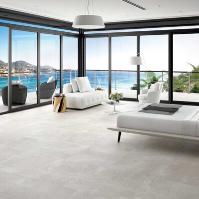 Dormitorio moderno con suelo de gres de color gris claro y acabado mate. La habitación tiene grandes ventanales con vistas al mar.