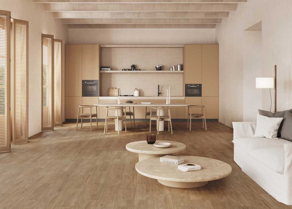 Amplio salón con cocina abierta y suelo porcelánico imitación madera. Muebles claros y ambiente cálido.