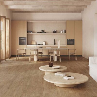 Amplio salón con cocina abierta y suelo porcelánico imitación madera. Muebles claros y ambiente cálido.