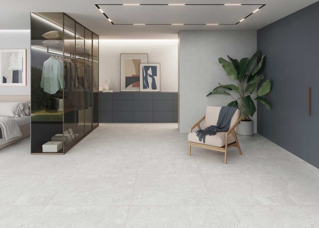Dormitorio moderno con suelo porcelánico de color gris claro y acabado mate. El espacio incluye un armario de cristal y una butaca.