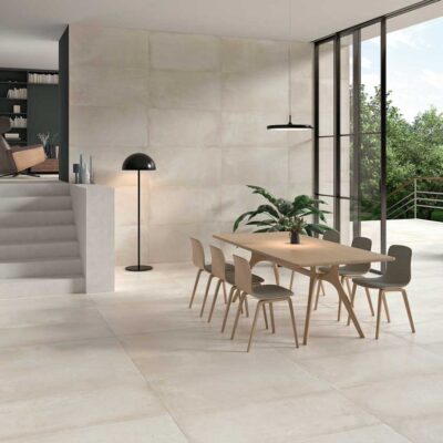 Suelo porcelánico Stoneage Sand en un comedor moderno con mesa de madera y ventanales.
