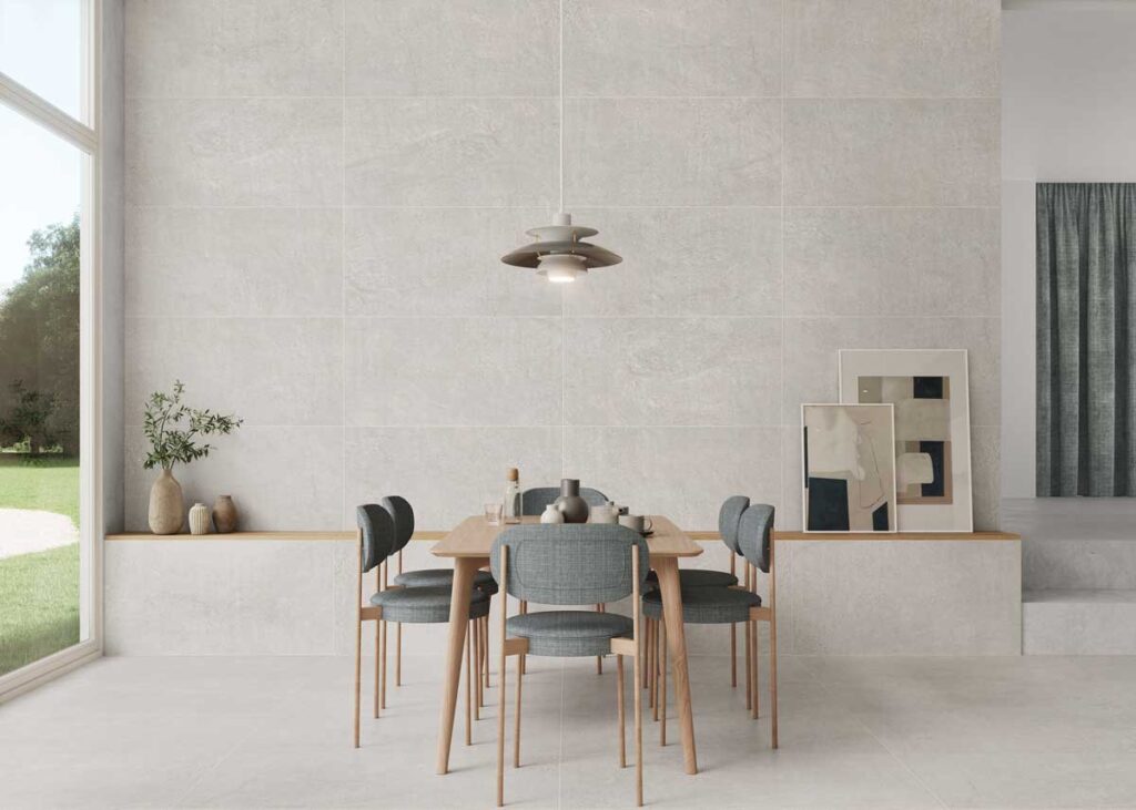 Moderno comedor con suelo porcelánico gris imitación piedra y pared a juego. Mesa de madera y sillas grises.