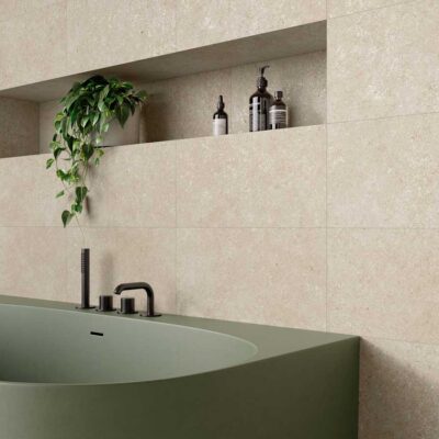 Pared de baño con azulejo porcelánico beige imitación piedra y bañera verde.