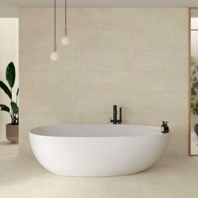 Baño moderno con paredes y suelo de porcelánico crema, bañera blanca y planta verde.
