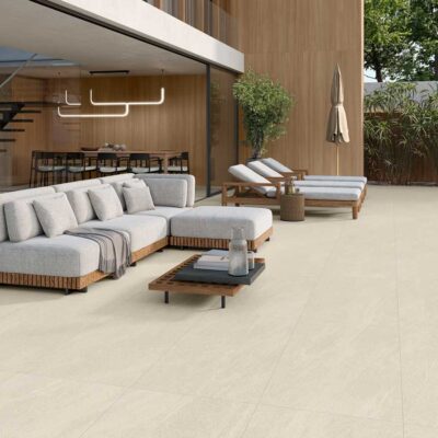 Amplia terraza exterior con suelo porcelánico Halton Cream, sofá, tumbonas y vegetación.