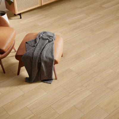 Suelo de porcelánico imitación madera Nuuk Roble en un salón con sillón de cuero.