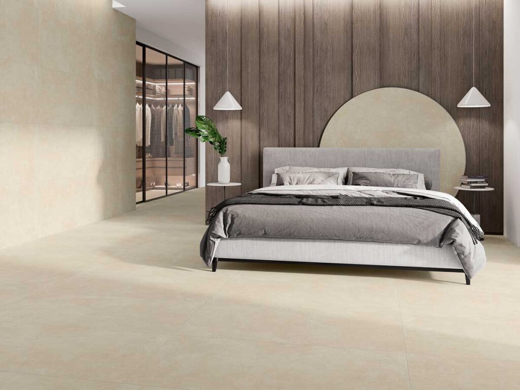 Dormitorio moderno con suelo porcelánico crema y pared a juego. Cama gris y armario de cristal.