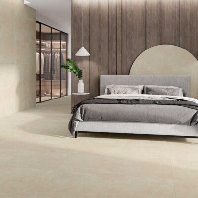 Dormitorio moderno con suelo porcelánico crema y pared a juego. Cama gris y armario de cristal.