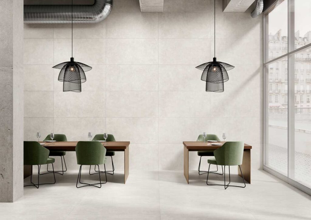 Sala moderna con suelo porcelánico imitación cemento Vanguard Pearl y paredes a juego. Mesas y sillas verdes.