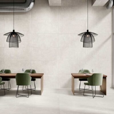 Sala moderna con suelo porcelánico imitación cemento Vanguard Pearl y paredes a juego. Mesas y sillas verdes.