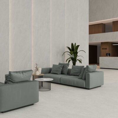 Amplio vestíbulo con suelo porcelánico Halton Grey y paredes a juego. Sofás grises y planta.