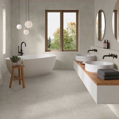 Suelo porcelanico Lomma Bone gris claro en un baño moderno con bañera y doble lavabo.