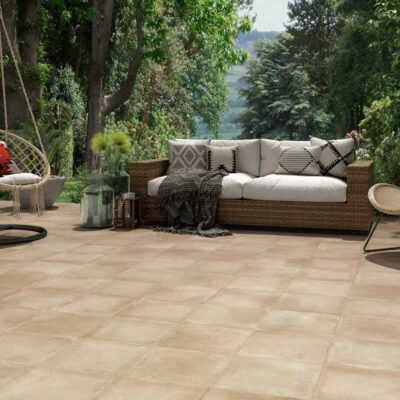 Patio exterior con suelo porcelánico imitación cemento Lecca Crema, rodeado de vegetación y mobiliario de jardín.