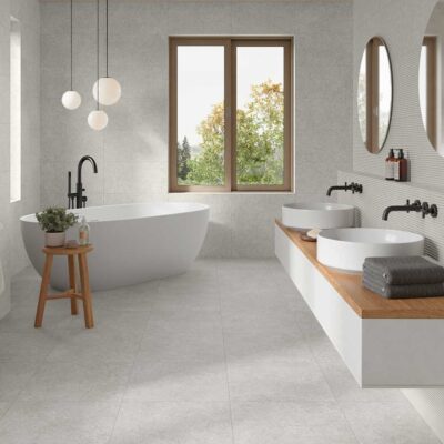 Baño luminoso con suelo porcelánico gris efecto piedra, bañera exenta y lavabos dobles.