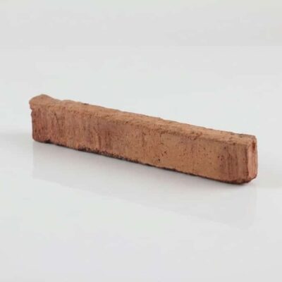 Pieza rectangular de barro cocido en tonalidad roja envejecida con superficie rugosa y acabado mate, formato alargado típico de complementos y zócalos rústicos.
