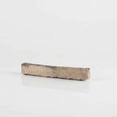 Pieza rectangular de baldosa cerámica rústica en tonos blancos y beige con superficie texturizada y acabado envejecido, mostrando bordes irregulares característicos del material.