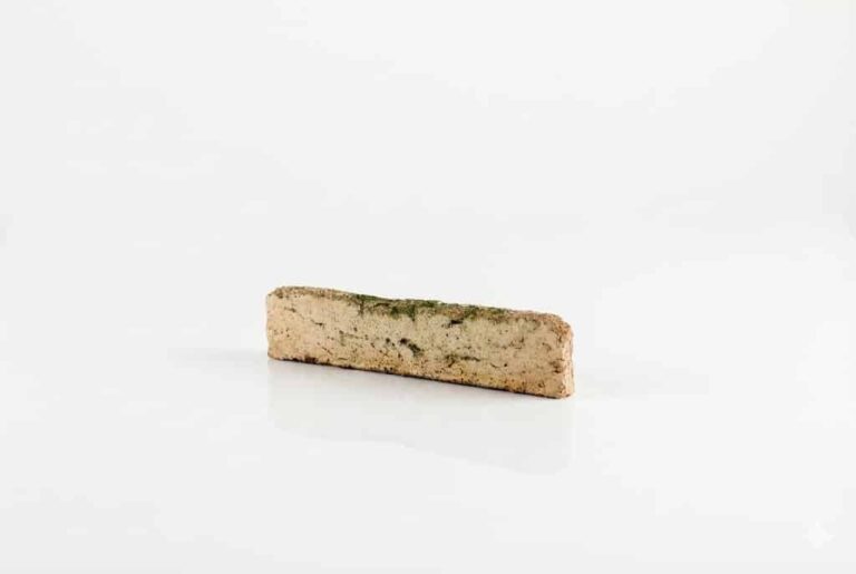 Pieza rectangular de baldosa cerámica con acabado enarenado en tonos beige y musgo, textura rugosa y superficie mate que imita piedra natural.