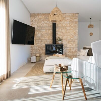 Salón contemporáneo con suelo de gres porcelánico en tonos claros, pared de ladrillo visto en color arena con chimenea integrada, y mobiliario blanco minimalista. Luz natural realza la calidez del espacio.