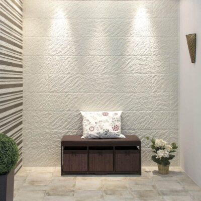 Recibidor con paredes revestidas de baldosa efecto piedra en tonos marfil y gris, banco de madera wengué con cojín estampado, plantas decorativas y apliques de iluminación empotrados.