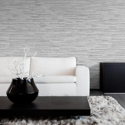Salón contemporáneo con paredes revestidas en gris texturado, sofá blanco ribeteado y suelo porcelánico imitación madera en tonos grises. Centro de mesa negro brillante con rama blanca decorativa sobre alfombra gris claro.