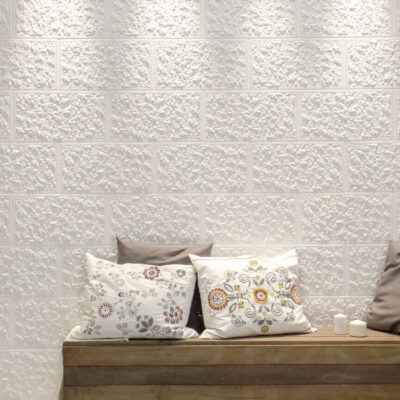 Salón contemporáneo con sofá gris y cojines estampados frente a pared revestida con paneles de revestimiento texturizado en tonos marfil y blanco crema, acabado mate con relieve tridimensional.