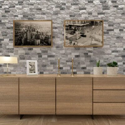 Ambiente interior con pared revestida con aplacado imitación piedra en tonos grises y blancos, mueble de madera clara inferior, y dos fotografías en blanco y negro enmarcadas en la parte superior.