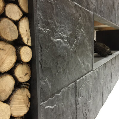 Pieza de aplacado con imitación de piedra pizarra en tonos gris oscuro, textura rugosa y acabado mate. Formato rectangular apilable con bordes naturales irregulares, diseñado para revestimiento de paredes.