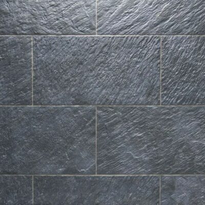 Superficie de gres porcelánico con textura de piedra natural en tonos gris oscuro y antracita, acabado mate rugoso que imita vetas y relieves característicos de la pizarra.