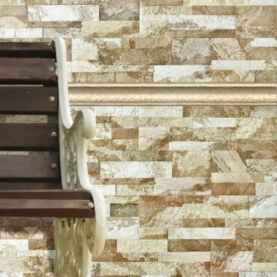 Pared interior revestida con gres porcelánico imitación piedra en tonos beige y crema, con piezas rectangulares en formato stacked. Escalera de madera oscura adosada a la izquierda. Acabado rústico con textura natural y variación cromática característica del efecto piedra.