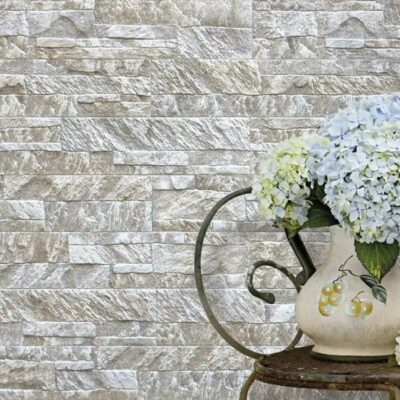 Pared con aplacado de hormigón imitación piedra en tonos grises y beige, decorada con jarrón de cerámica blanca con flores de hortensia azul y blanca sobre una superficie de madera oscura.