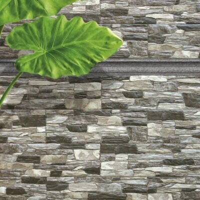 Revestimiento de pared con aplacado de gres cerámico en tonos grises y beige, con textura y acabado que imita piedra natural. Detalle de hojas verdes de planta decorativa sobre la superficie.
