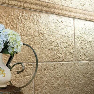 Revestimiento de pared con gres cerámico de acabado texturizado en tonos ocre y beige, junto a una jarra decorativa de cerámica blanca con flores azules y detalles de cerámica amarilla.