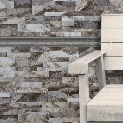 Baldosas rectangulares de gres cerámico en tonos grises y beige con efecto piedra natural y textura rugosa, dispuestas en patrón de rejuntado irregular. Las piezas muestran variaciones de color y veteado característico del suelo de gres.