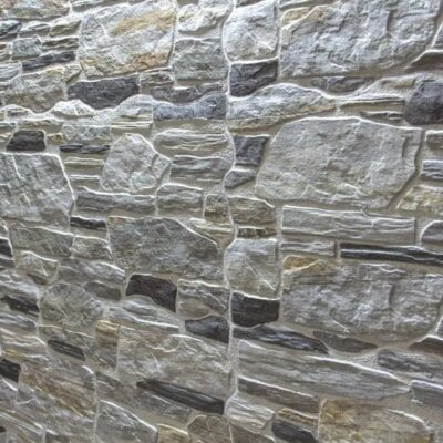 Superficie de gres cerámico con textura de piedra irregular en tonos grises y beige, acabado mate rústico. Las piezas presentan relieve natural y variación cromática típica de suelos porcelánicos efecto piedra.