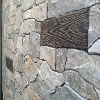 Aplacado de pared con dos materiales contrastados: a la izquierda, baldosa de gres cerámico gris con acabado natural y textura irregular; a la derecha, franja de madera oscura con veteado visible. Detalle de instalación que muestra cómo combinar suelo cerámico con elementos de madera.
