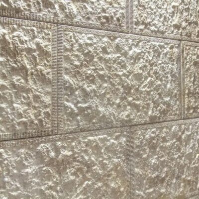 Superficie de gres cerámico con textura rugosa imitación piedra en tonos beige y gris claro, acabado mate con relieve natural y veteado irregular.