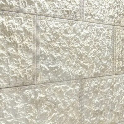 Superficie de gres cerámico con textura rugosa y acabado mate en tonos beige y gris claro, mostrando detalles de relieve y variaciones de color naturales del material.