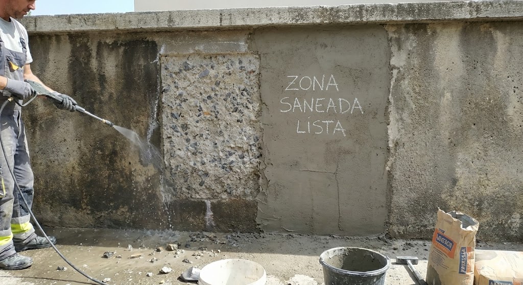 Limpieza y reparación de muro de hormigón exterior antes de decorar, con zona saneada lista para acabado