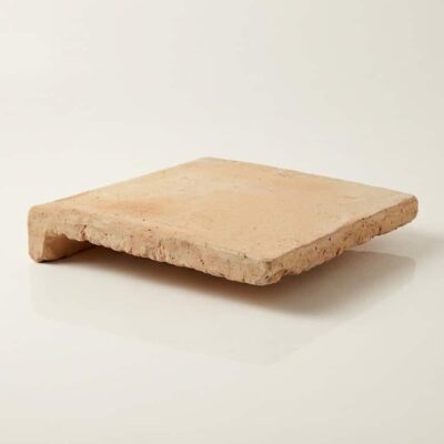 Peldaño de barro natural cuadrado con superficie rústica en tonos beige y acabado mate. Pieza irregular con bordes naturales y textura porosa característica del material de terracota.